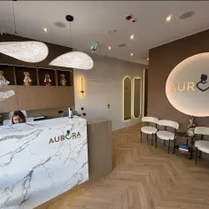 Recepcja kliniki medycznej Aurora Medical z marmurowym blatem, siedzącą recepcjonistką i logo.