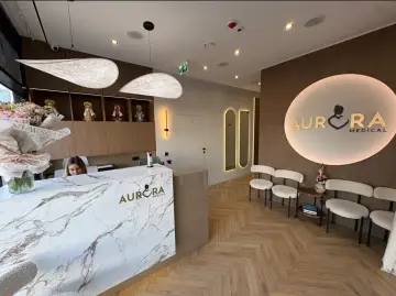 Recepcja kliniki medycznej Aurora Medical z marmurowym blatem, siedzącą recepcjonistką i logo.